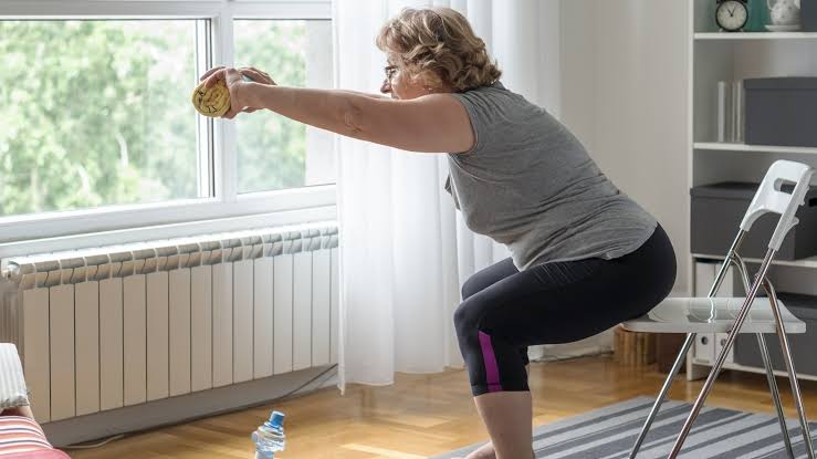 Older woman practicing a supported chair squat at home beside a sturdy chair